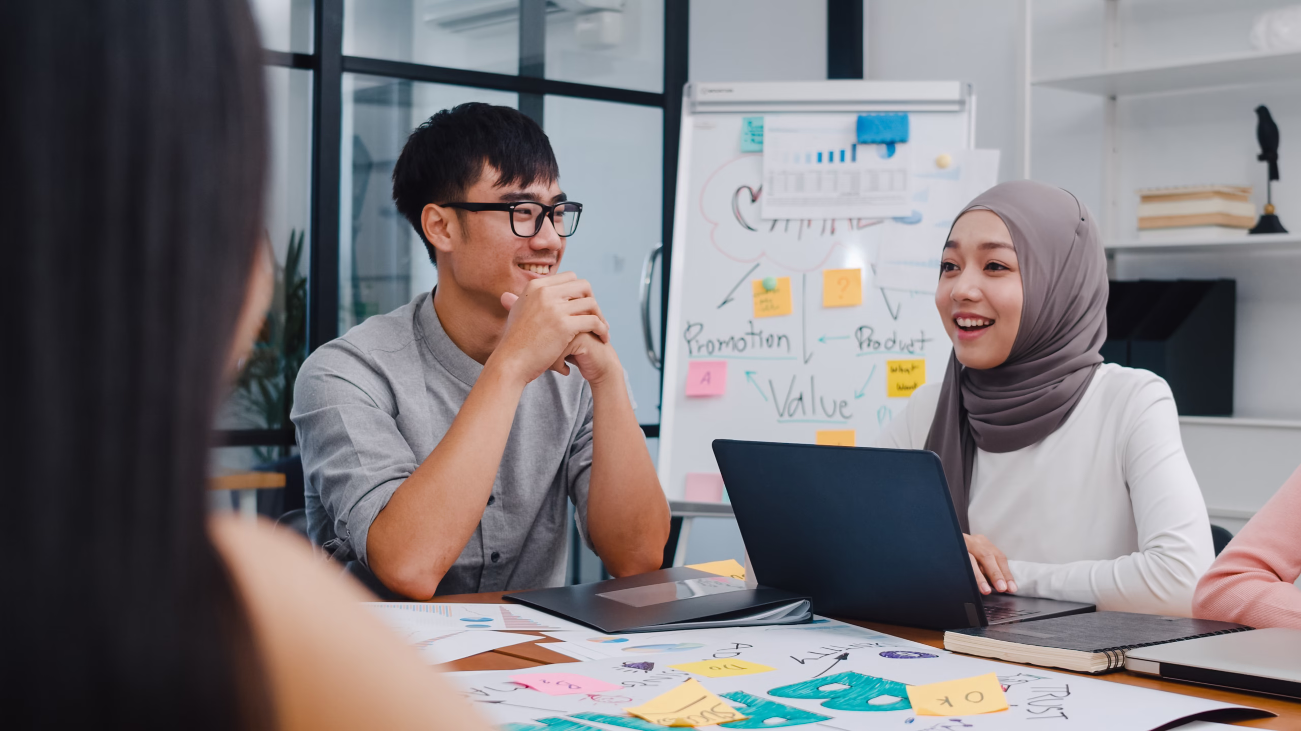 Tim bisnis muda sedang berdiskusi di kantor modern dengan papan strategi, menggambarkan pertimbangan dalam memilih badan usaha sesuai kebutuhan, termasuk perbedaan PT Biasa dan PT Perorangan.