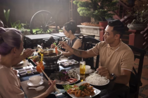 Sekelompok orang Asia menikmati makan malam bersama di restoran, dengan hidangan hotpot, mi, dan makanan laut di meja.\n\nCaption gambar: Suasana hangat makan malam bersama teman di restoran dengan hidangan hotpot, mi, dan seafood yang menggugah selera.
